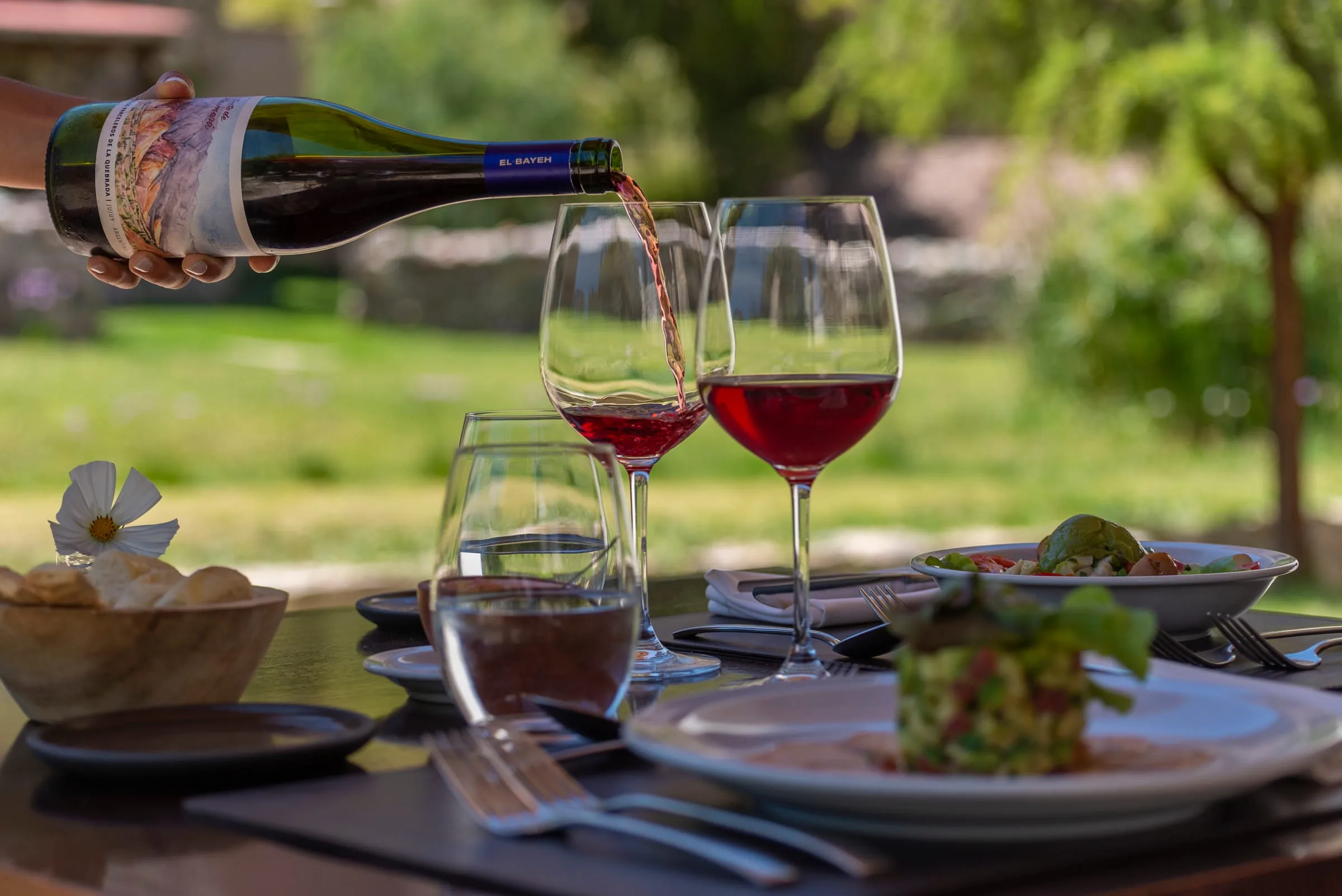 Copas de vino tinto servidas en una mesa al aire libre, con el parque del hotel de fondo