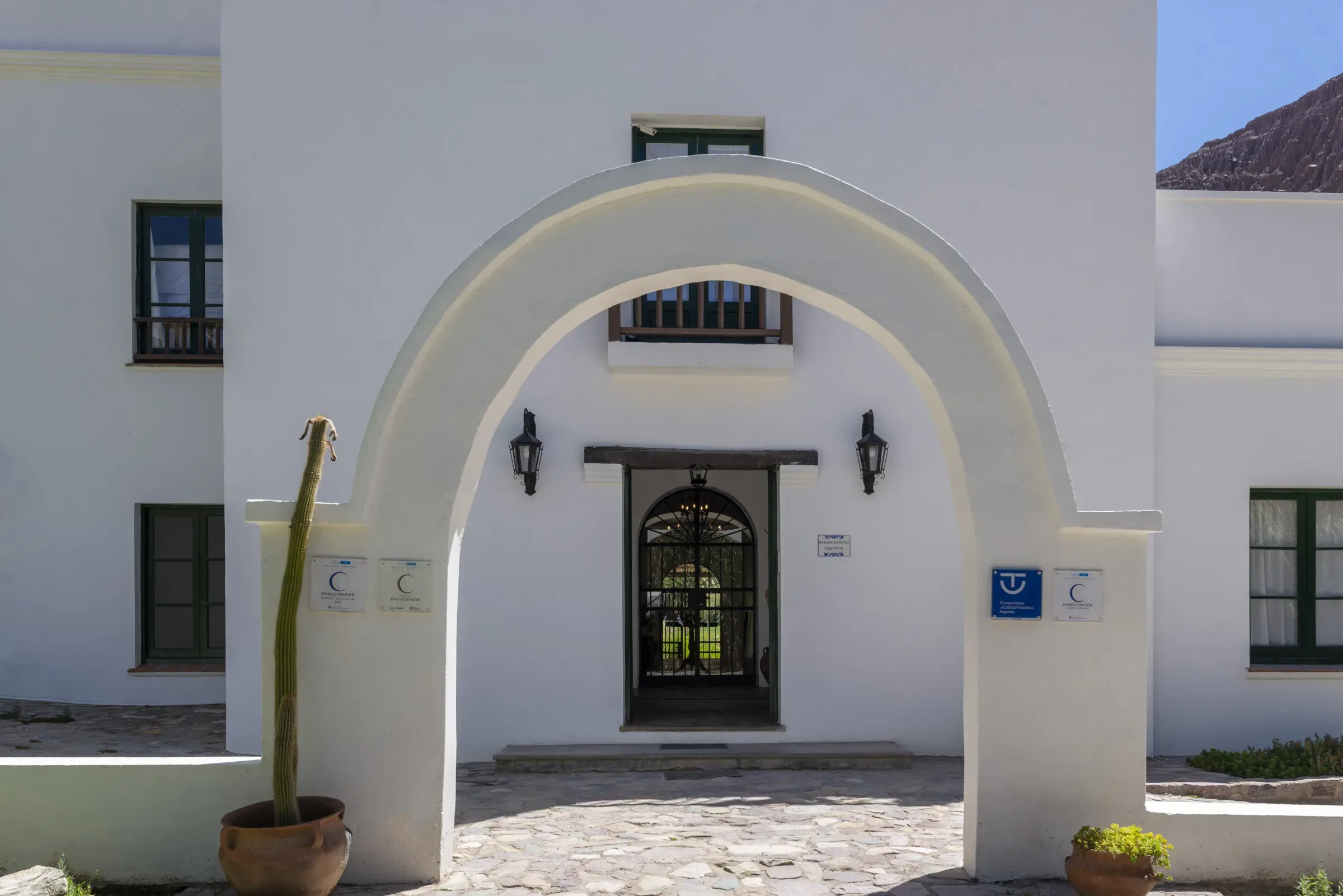 El arco de entrada encalado, con faroles de hierro y un cardón en maceta de barro
