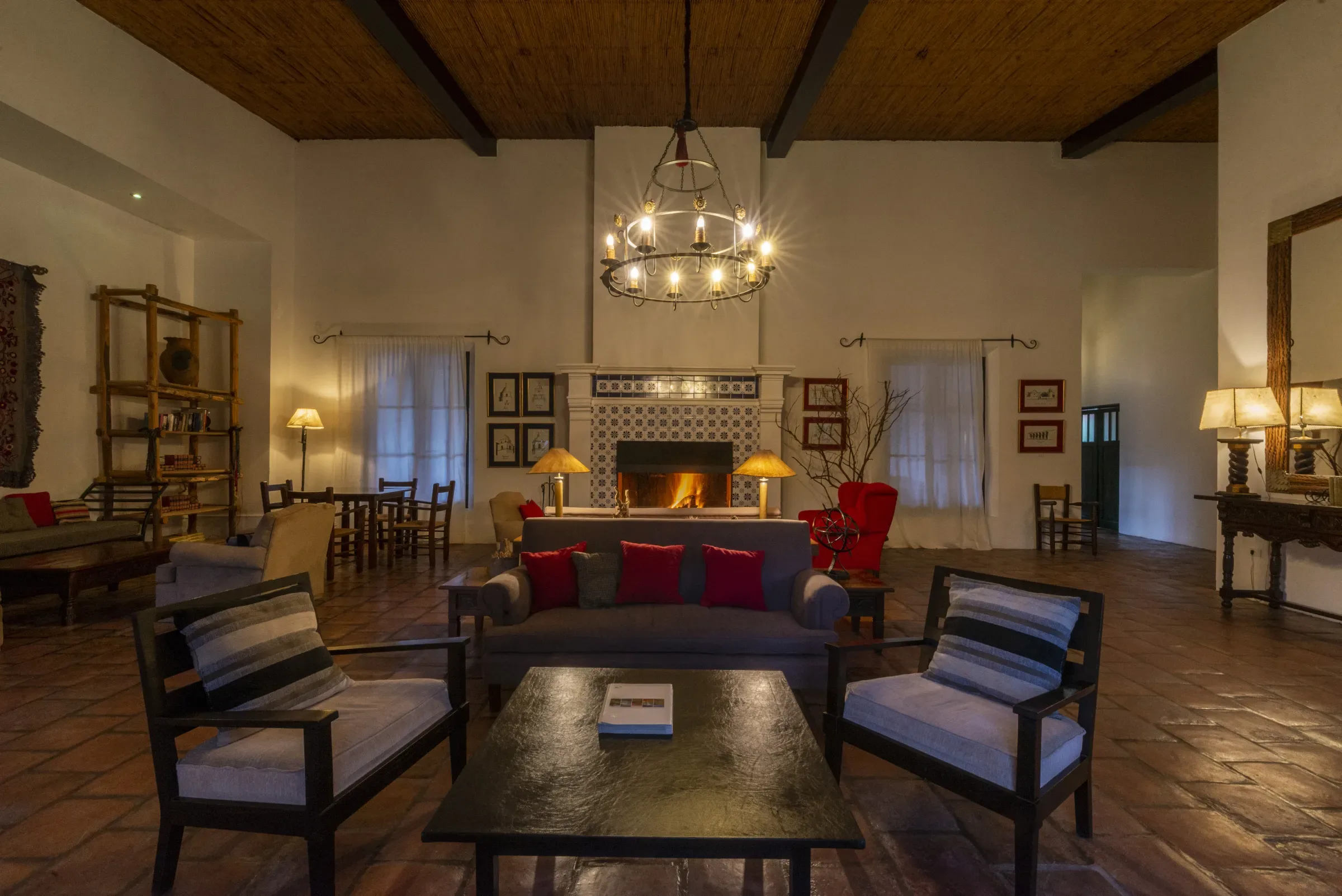 Sala de estar con chimenea encendida, araña de hierro y piso de terracota