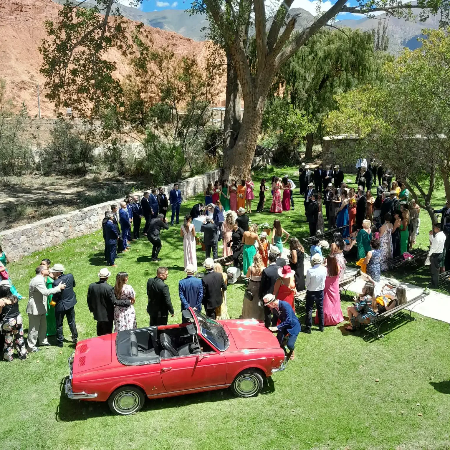 Invitados de una boda alrededor de un auto clásico rojo en el parque