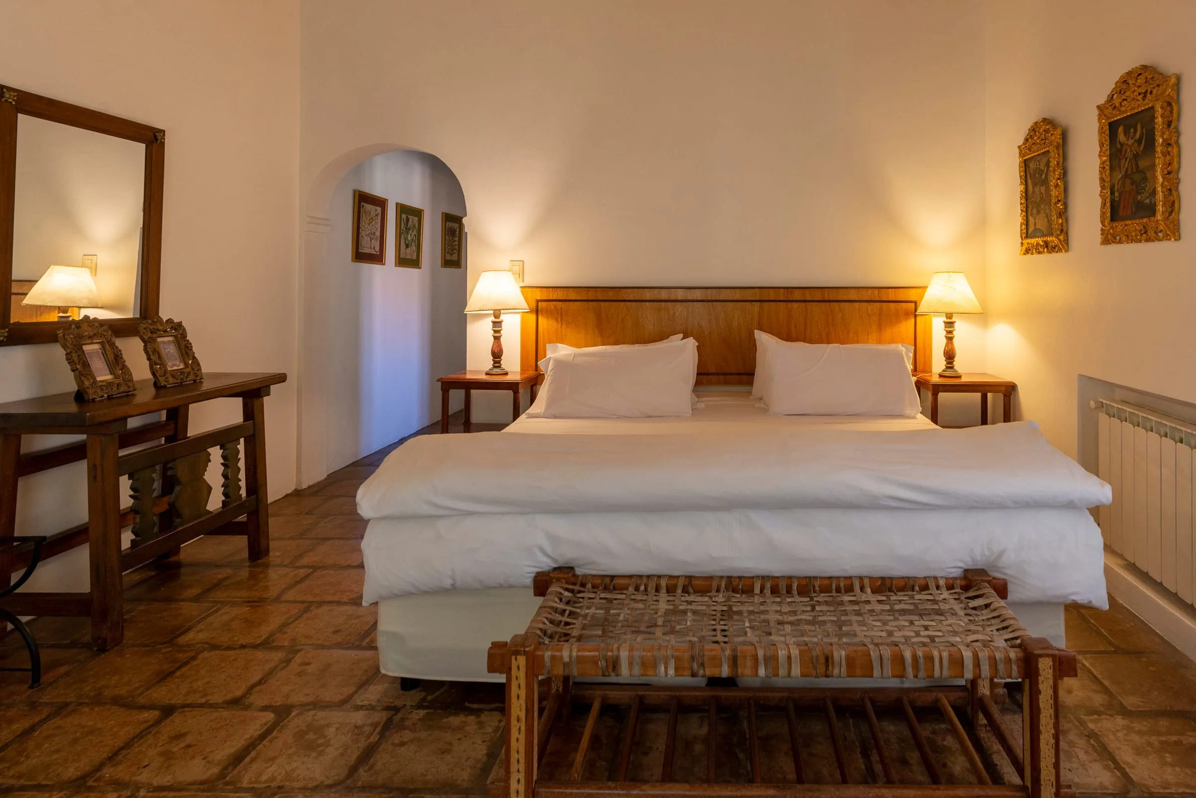 Habitación doble con cabecera de madera tallada, veladores encendidos y piso de terracota