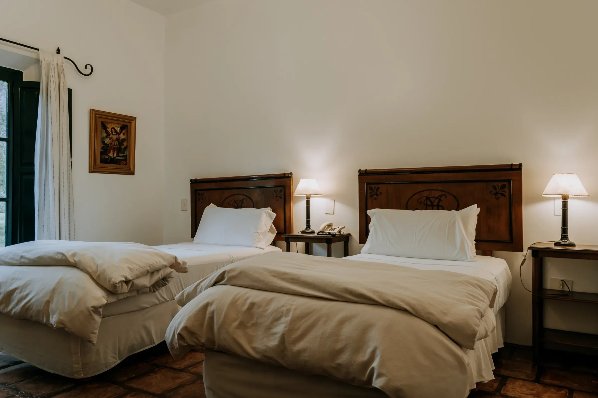 Habitación twin con dos camas, cabeceras talladas y postigos verdes